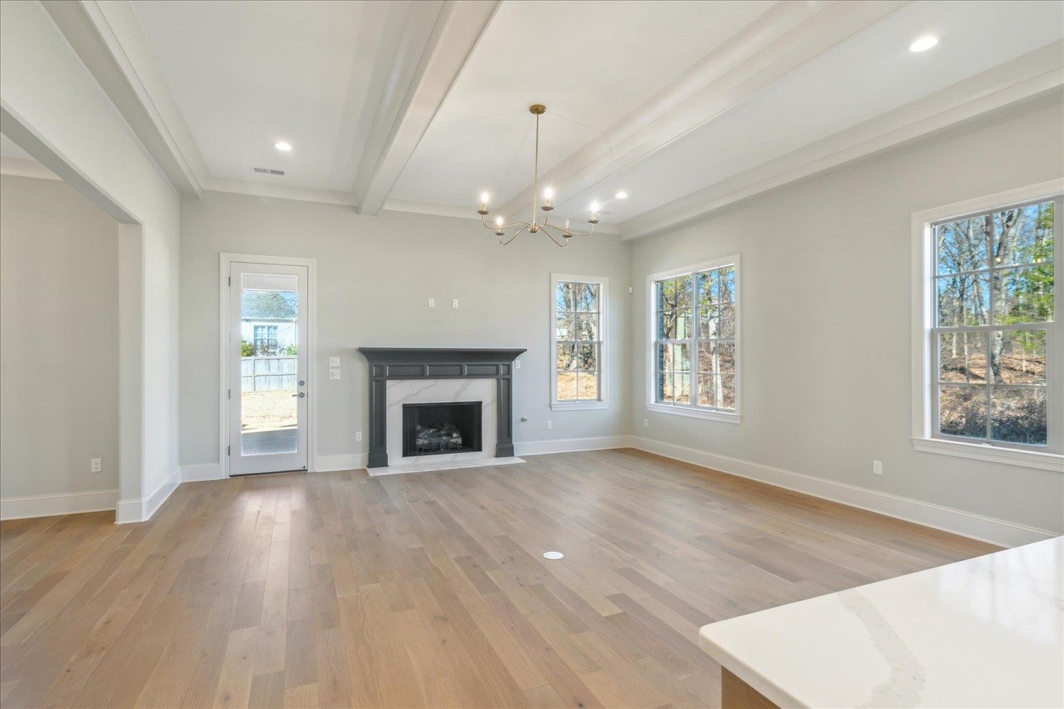 12620 Miss Cloud Road Collierville, TN 38017 - Photo 8 of 38 Unfurnished living room with light hardwood / wood-style floors, a premium fireplace, a chandelier, and beamed ceiling
