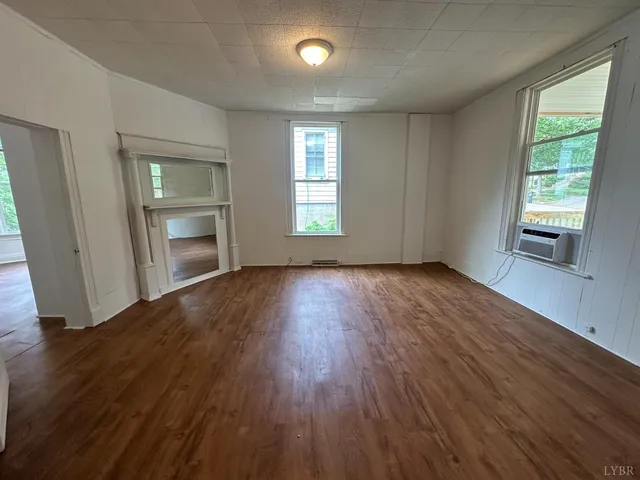 an empty room with wooden floor fireplace and windows