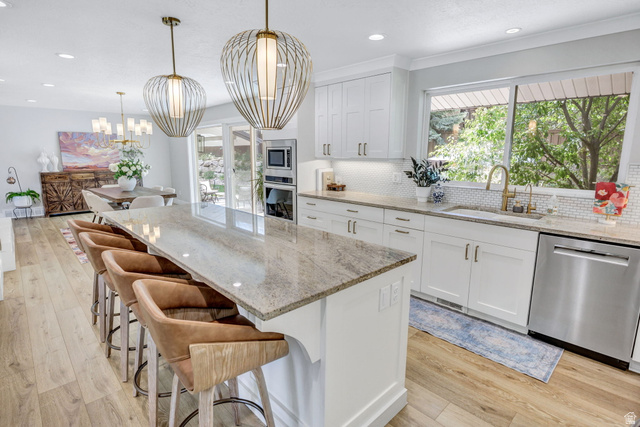 1350 Canyon Park Road Bountiful, UT 84010 - Photo 12 of 38 Open-concept kitchen featuring a large island with seating, pendant lighting, white cabinetry, a tiled backsplash, and stainless steel appliances