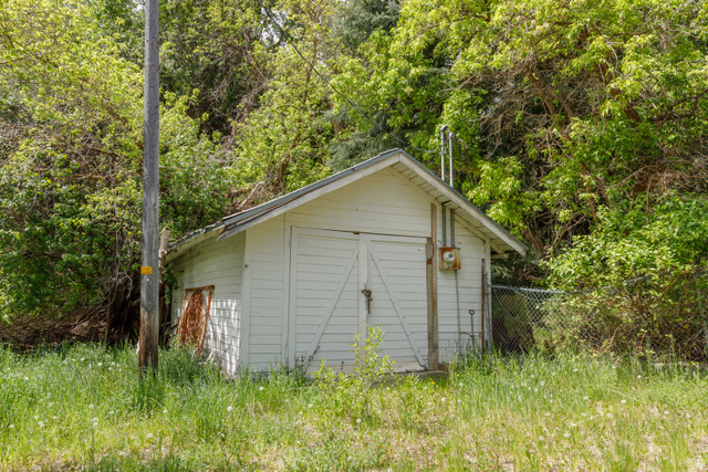 6449 North North Fork Road Eden, UT 84310 - Photo 7 of 38 White horizontal siding structure with a pitched roof and double front doors, surrounded by mature trees and overgrown grass