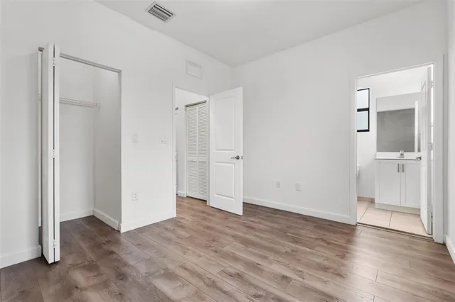 a view of an empty room with wooden floor and a bathroom