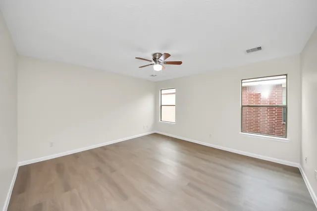 an empty room with wooden floor chandelier fan and windows