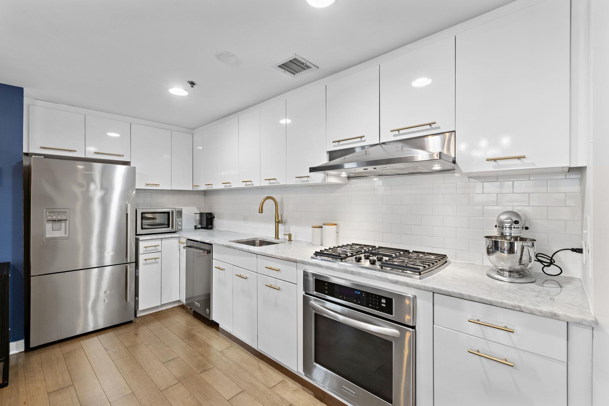 609 Observer Highway, Unit 303 Hoboken, NJ 07030 - Photo 6 of 20 a kitchen with stainless steel appliances granite countertop a sink stove a refrigerator and white cabinets with wooden floors