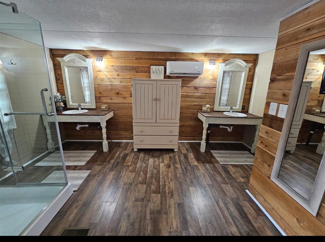 390 Wharf Road Savannah, TN 38372 - Photo 3 of 17 Bathroom featuring wood-finish flooring, a glass-enclosed shower, dual vanity sinks with framed mirrors, a central storage cabinet, and wood paneling