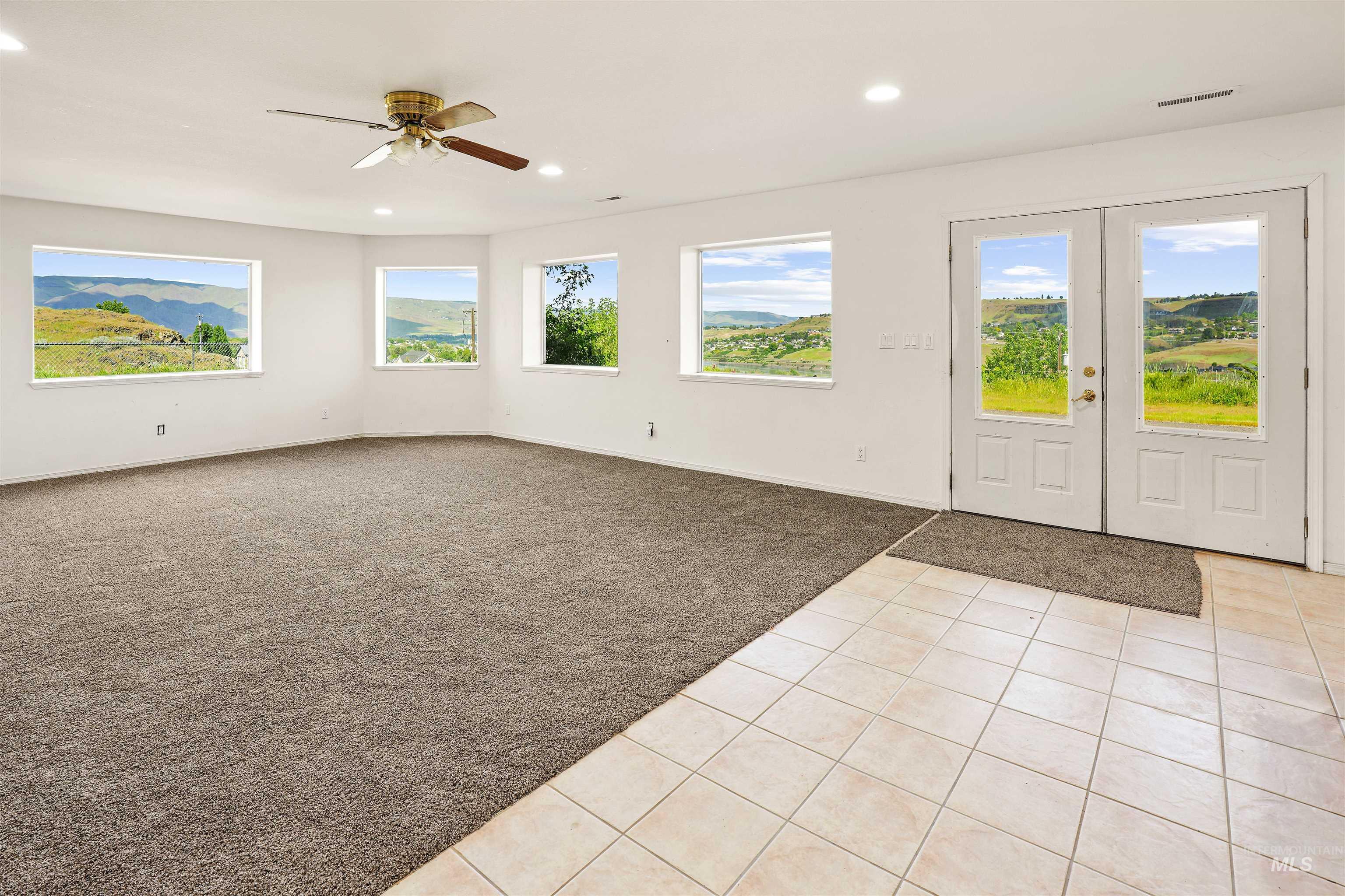2750 South Perry Lane Clarkston, WA 99403 - Photo 36 of 47 Spacious room featuring broad windows with framed scenery, a two-tone flooring of plush carpeting and light-toned square tile, recessed ceiling lighting, a brass-finish ceiling fan, and white French doors
