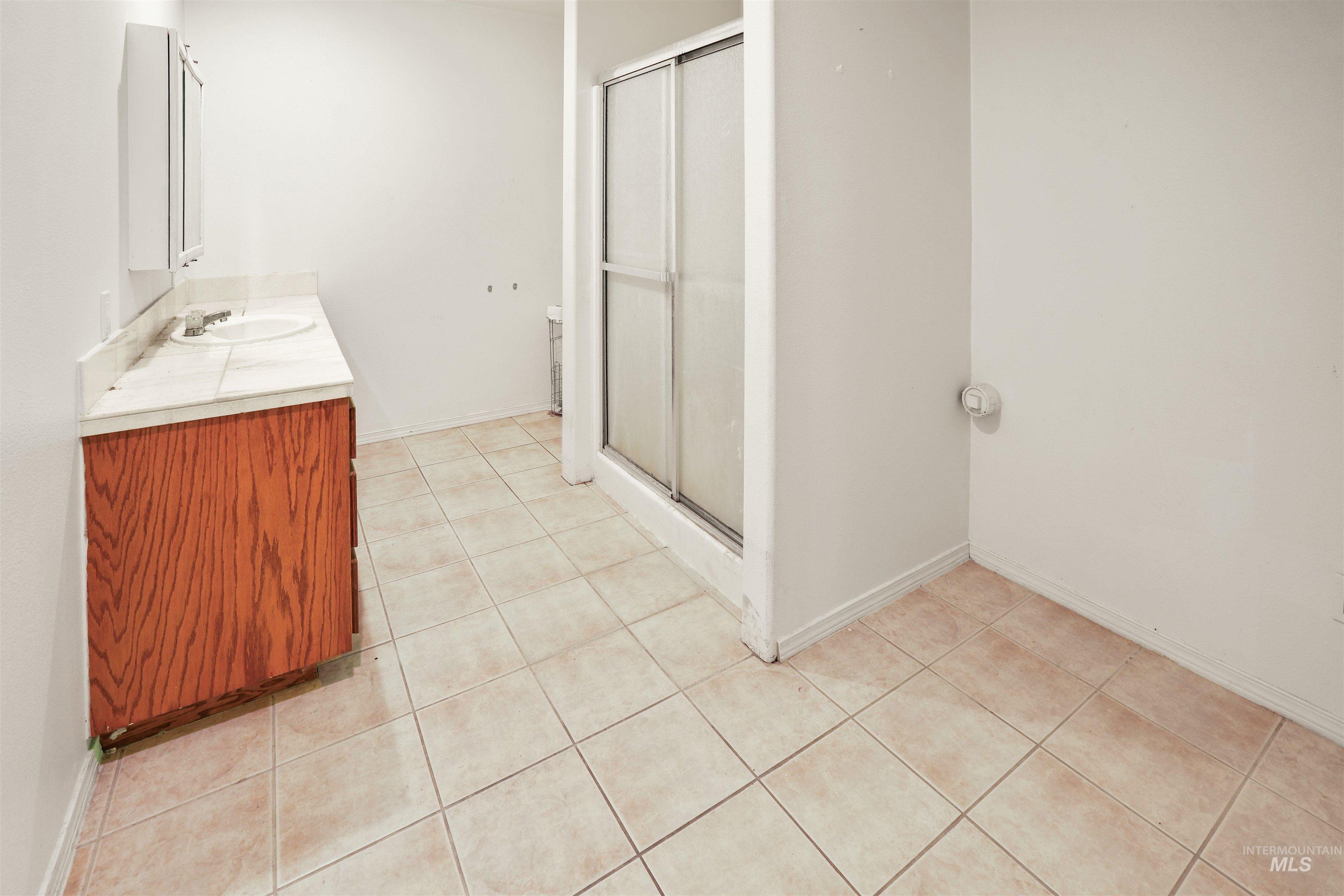 2750 South Perry Lane Clarkston, WA 99403 - Photo 45 of 47 Bathroom featuring a single vanity with wood-finish cabinetry and a light-toned countertop, a frameless mirror, a shower stall with a sliding glass door, and square floor tiling throughout