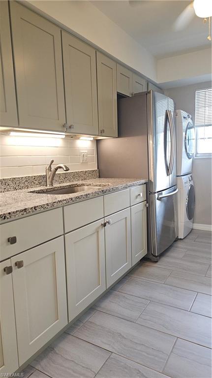 4900 Biscayne Drive, Unit 23 Naples, FL 34112 - Photo 6 of 21 Kitchen with stacked washer and dryer, sink, light stone counters, refrigerator, and backsplash