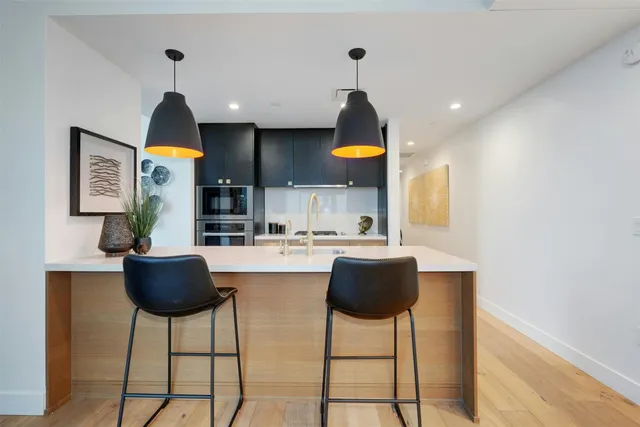 a kitchen with stainless steel appliances kitchen island granite countertop a refrigerator a stove a dining table and chairs with wooden floor