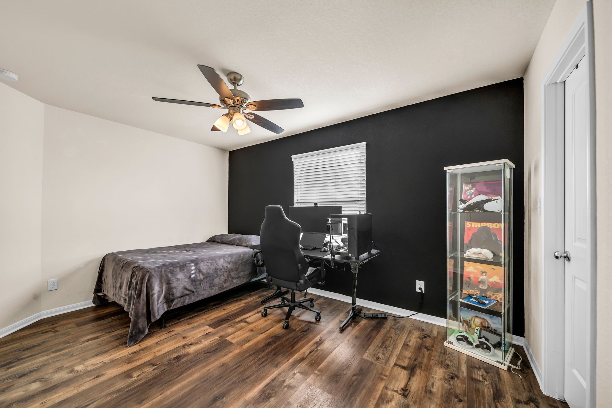 14212 Portrait Court Houston, TX 77045 - Photo 21 of 27 Spacious bedroom featuring a sleek black accent wall, warm wood-like flooring, and abundant natural light—ideal for relaxation or a home office setup.