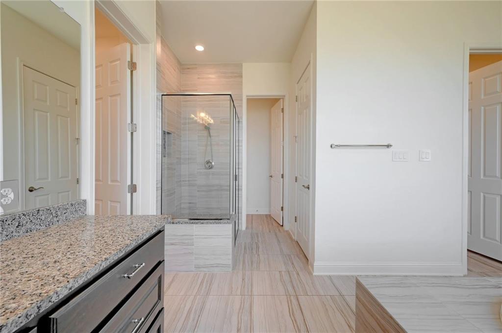 168 Raton Pass Dripping Springs, TX 78620 - Photo 15 of 20 Spacious bathroom featuring a glass-enclosed shower with tile surround, wood-finish flooring, and a vanity with a granite-style countertop