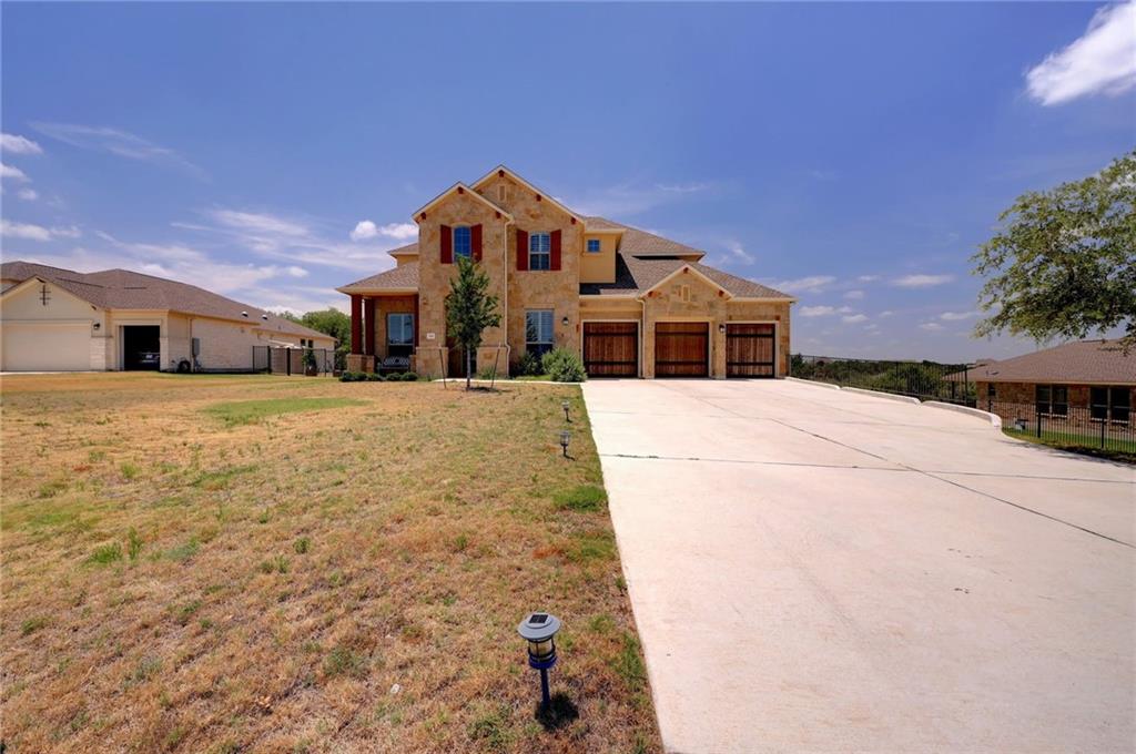 168 Raton Pass Dripping Springs, TX 78620 - Photo 2 of 20 Two-story stone and stucco exterior home with a columned front porch, red shutters, and a three-car garage featuring wood-finish doors