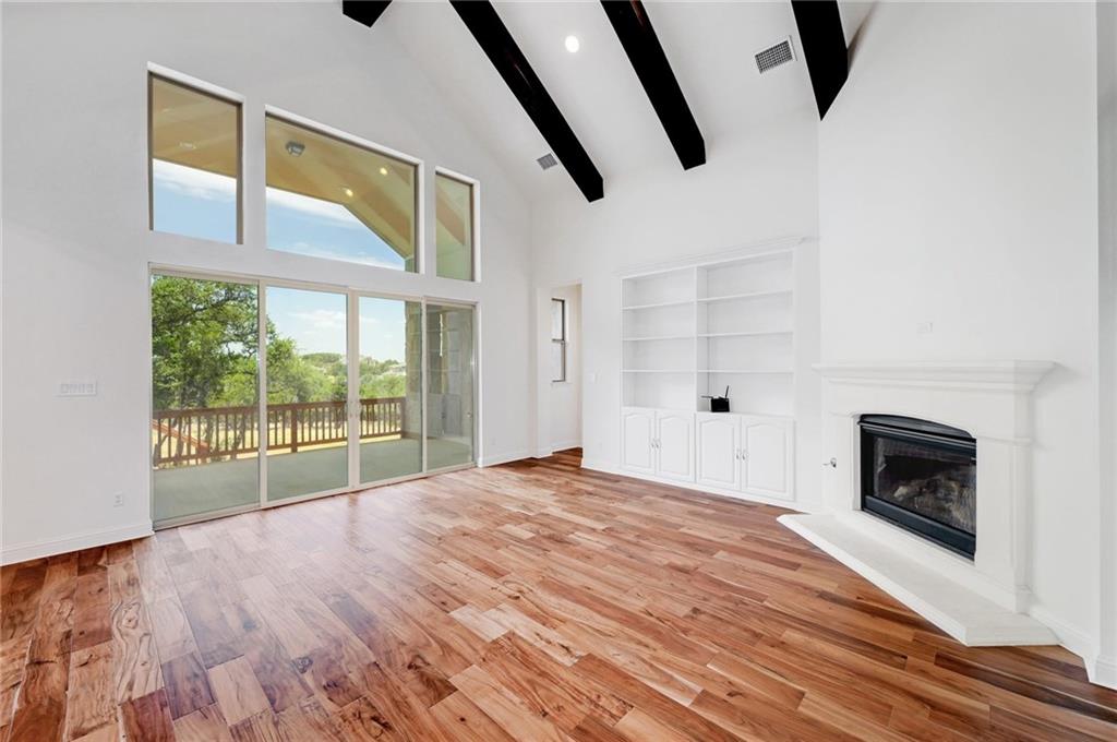 168 Raton Pass Dripping Springs, TX 78620 - Photo 5 of 20 Vaulted ceilings with exposed beams, wood-finish flooring, a built-in fireplace with a hearth, integrated shelving, and large sliding glass doors opening to a balcony
