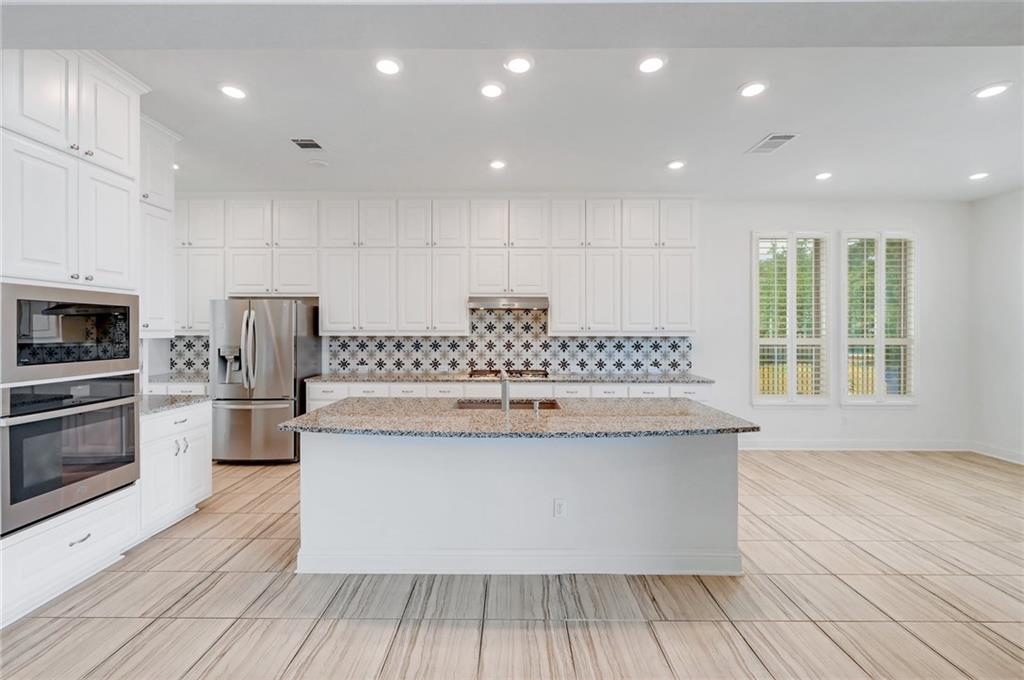 168 Raton Pass Dripping Springs, TX 78620 - Photo 9 of 20 Spacious kitchen featuring an expansive center island with stone countertop, white cabinetry with contemporary hardware, full stainless steel appliance suite, patterned tile backsplash, and light wood-finish flooring