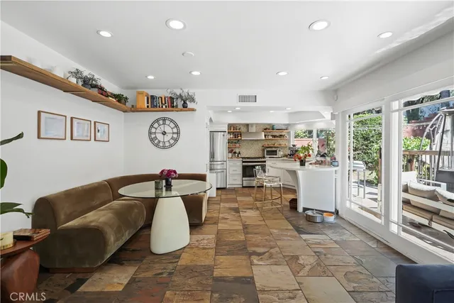 a living room with stainless steel appliances furniture a rug kitchen view and a large window