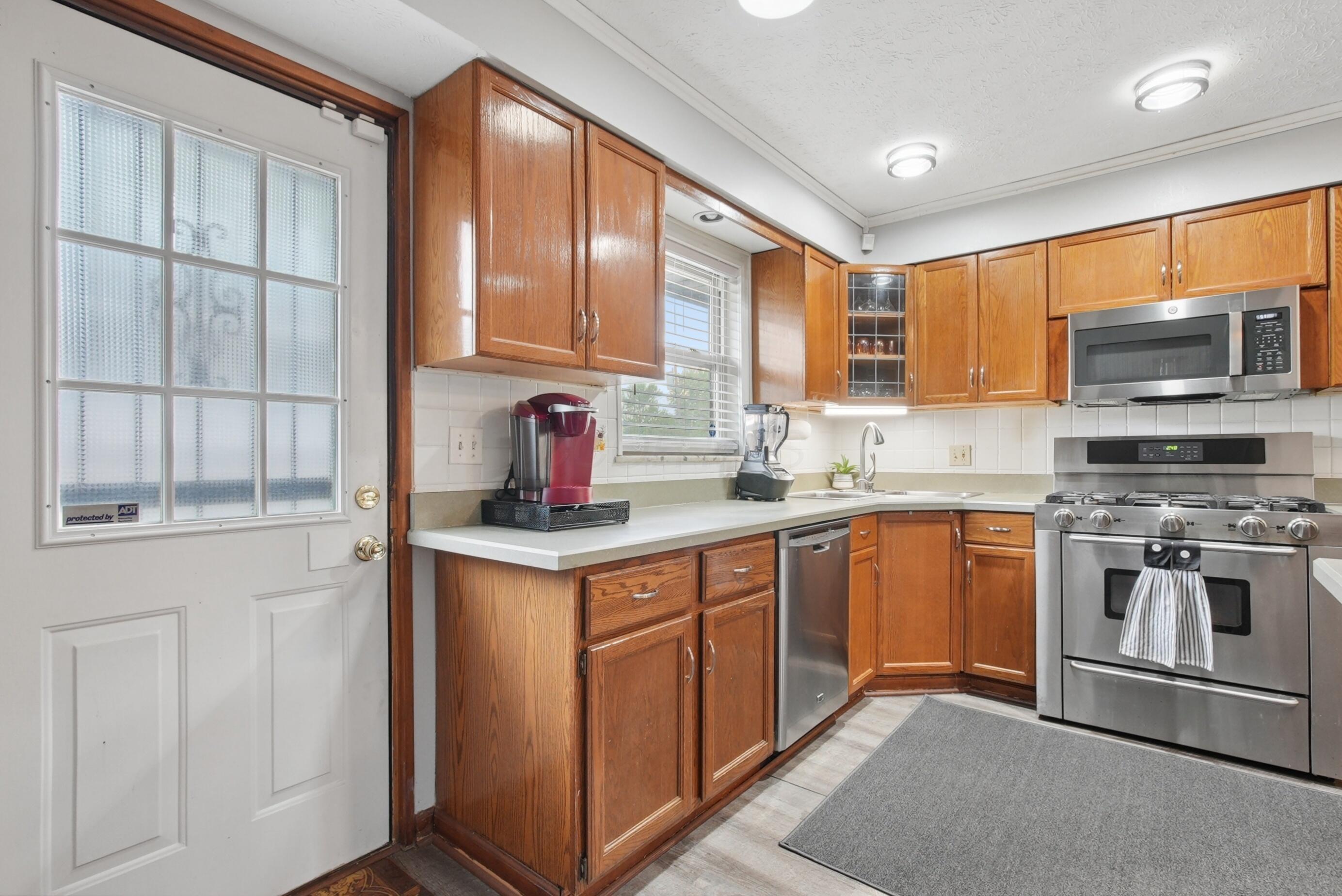 Kitchen featuring wood-finish cabinetry, stainless steel appliances, light-toned countertops, and a full tile backsplash