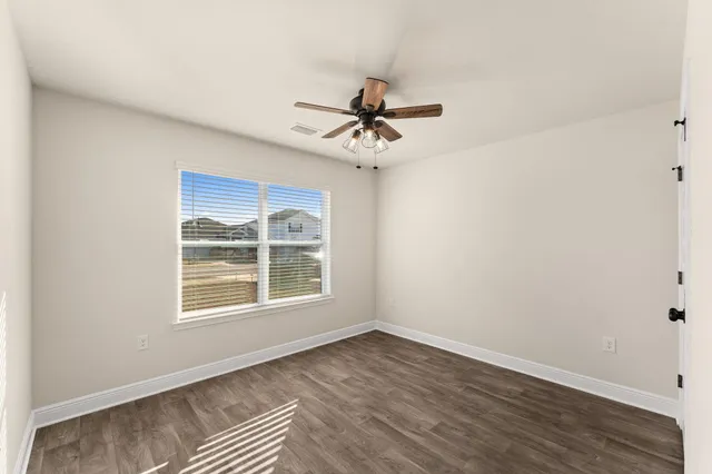 an empty room with wooden floor ceiling fan and windows