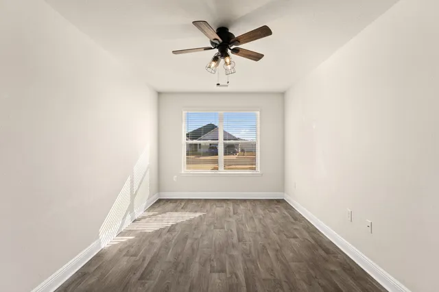 an empty room with wooden floor fan and windows