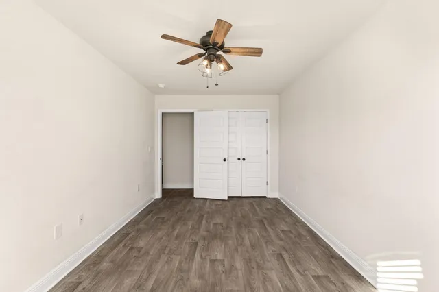 an empty room with wooden floor closet and fan