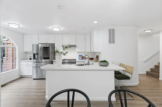 a kitchen with stainless steel appliances a sink a stove a refrigerator cabinets and a dining table with wooden floor