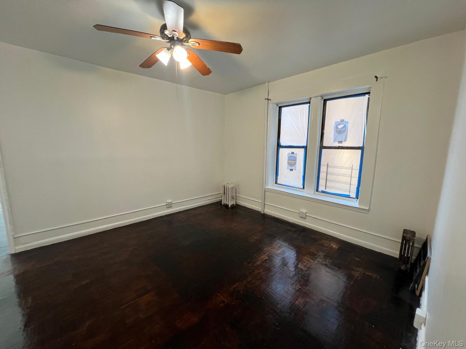 97-52 75th Street, Unit B1 Queens, NY 11416 - Photo 17 of 19 Empty room with dark wood-style floors, radiator heating unit, and ceiling fan