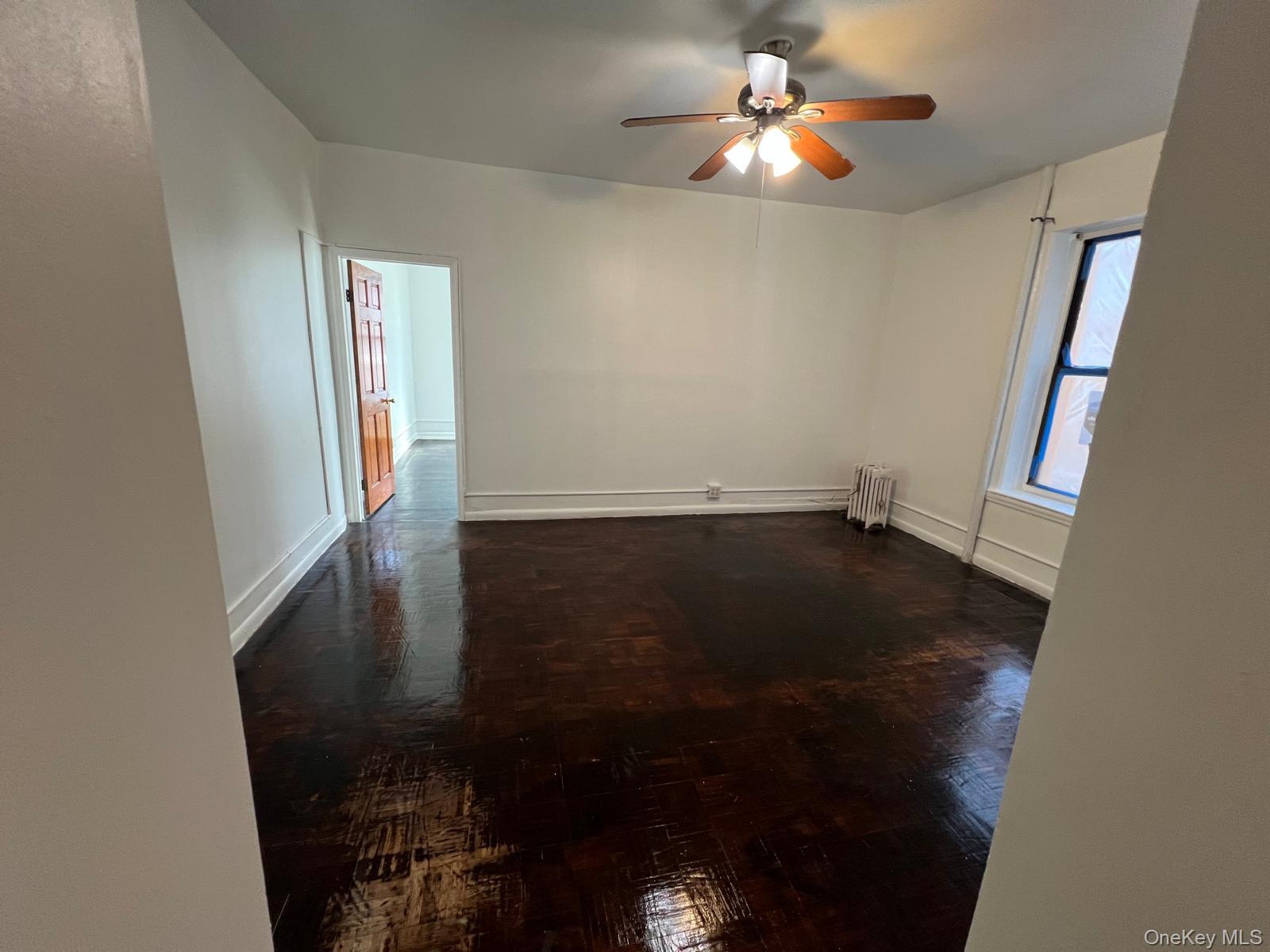 97-52 75th Street, Unit B1 Queens, NY 11416 - Photo 18 of 19 Unfurnished room with dark wood-style floors, ceiling fan, and radiator