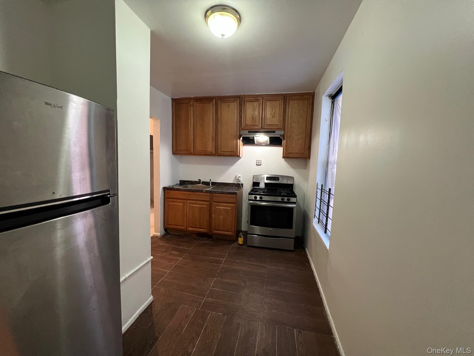 97-52 75th Street, Unit B1 Queens, NY 11416 - Photo 6 of 19 Kitchen featuring stainless steel appliances, brown cabinets, under cabinet range hood, and dark wood-type flooring