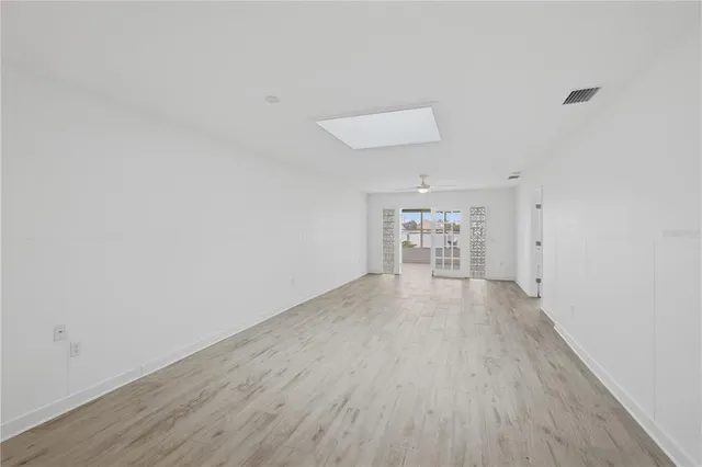 a view of an empty room and a kitchen with wooden floor