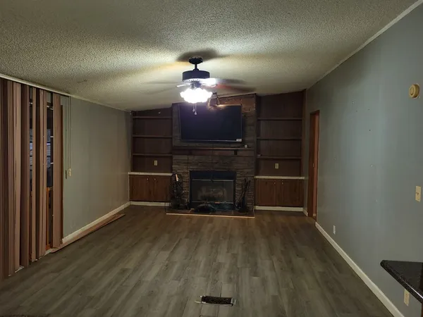 a view of a livingroom with a fireplace a ceiling fan and wooden floor