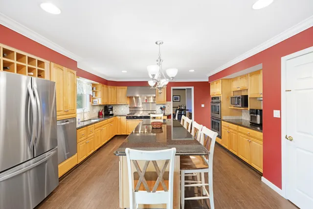 a kitchen with stainless steel appliances granite countertop a refrigerator a oven a sink and a dining table with wooden floor