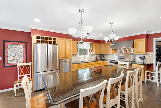 a kitchen with stainless steel appliances granite countertop a stove a refrigerator a kitchen island a dining table and chairs