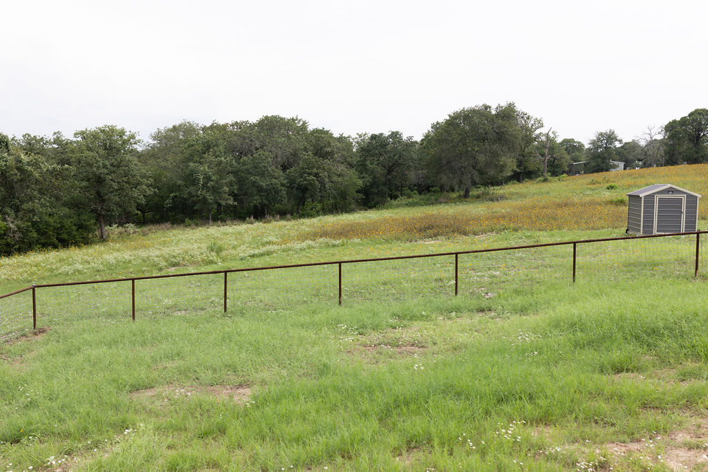 111 Powder Ridge Luling, TX 78648 - Photo 19 of 22 A rustic fence defines the boundary of a sprawling, verdant landscape with scattered wildflowers.