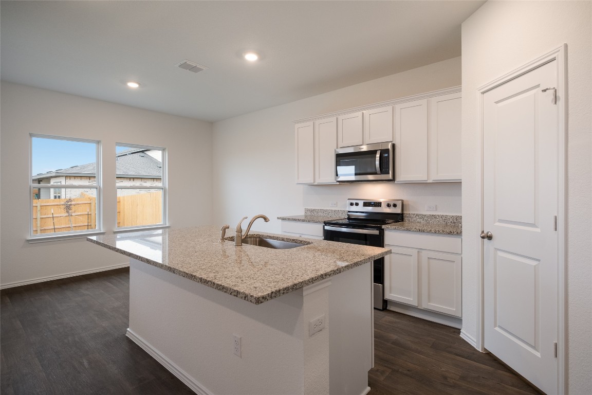 15009 Welsh Cob St Manor, Unit A Manor, TX 78653 - Photo 11 of 24 a kitchen with granite countertop stainless steel appliances a stove a sink a refrigerator and a granite counter tops with wooden floors
