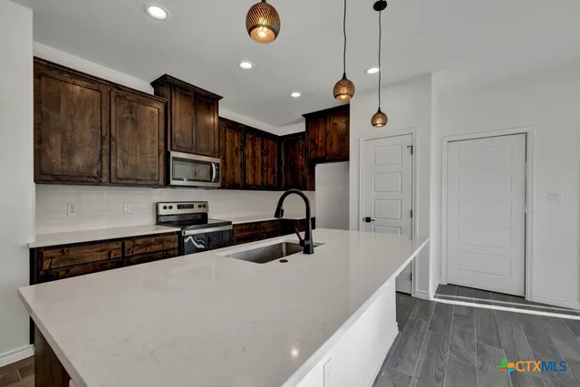 a kitchen with stainless steel appliances a sink a stove a refrigerator cabinets and a wooden floor