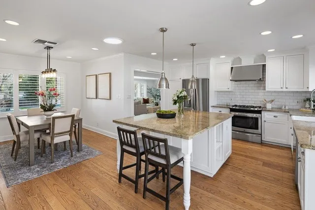 a kitchen with stainless steel appliances granite countertop a stove a refrigerator a kitchen island a dining table and chairs with wooden floor
