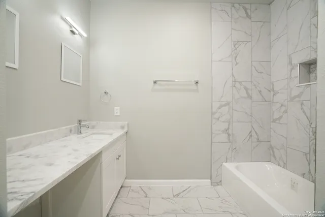 a bathroom with a granite countertop sink and mirror with bathtub
