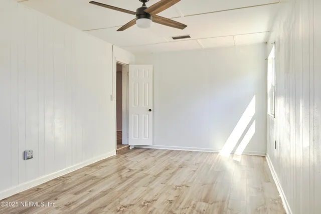 an empty room with wooden floor fan and windows