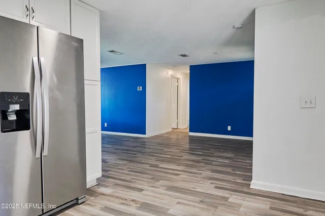 a view of an empty room with wooden floor and a refrigerator