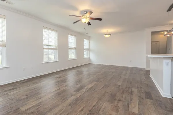an empty room with wooden floor chandelier fan and windows