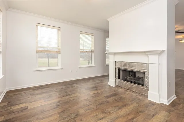 an empty room with wooden floor fireplace and windows