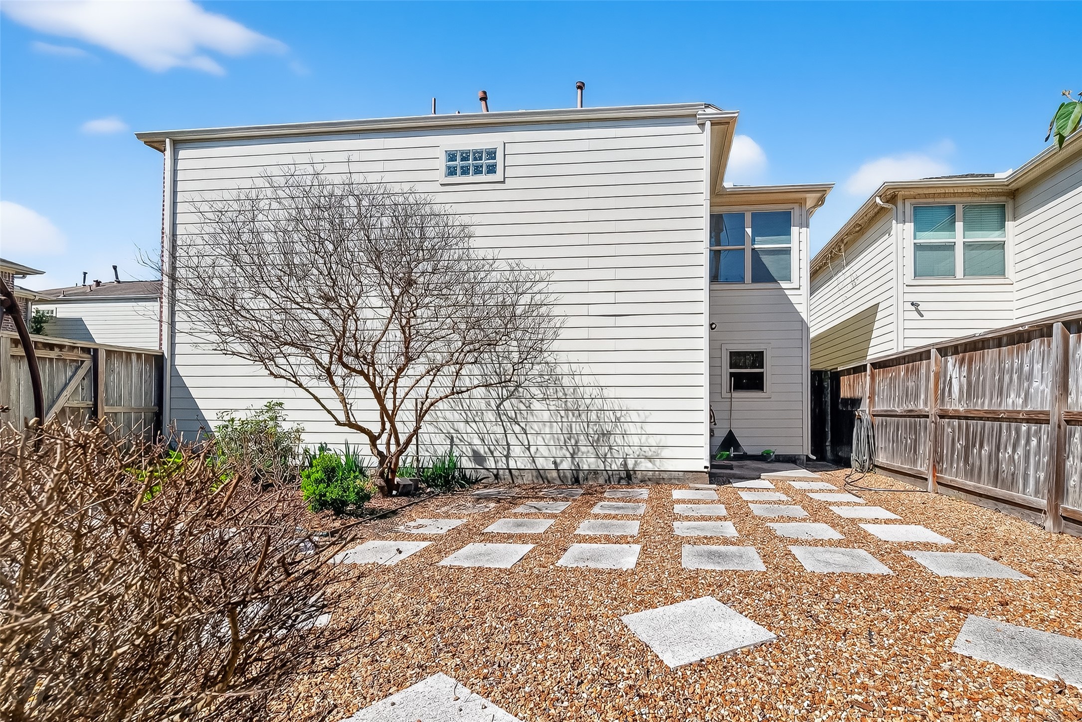 5951 S Loop East, Unit 47 Houston, TX 77033 - Photo 35 of 37 This backyard features a low-maintenance gravel area with stepping stones, bordered by a wooden fence. It includes a mature tree and some greenery, offering a private outdoor space adjacent to the house.