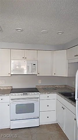 a kitchen with granite countertop white cabinets and white appliances