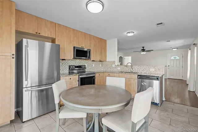 a kitchen with stainless steel appliances granite countertop a refrigerator a stove a sink a dining table and chairs