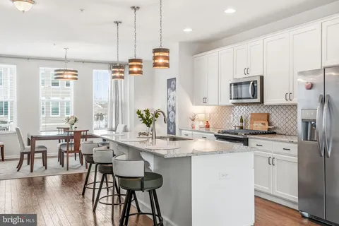 a kitchen with stainless steel appliances granite countertop a stove a sink a microwave a refrigerator and white cabinets with wooden floor