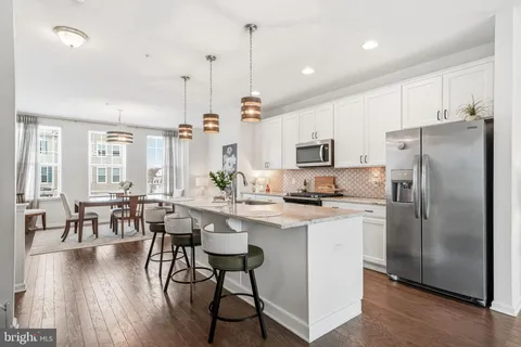a kitchen with stainless steel appliances granite countertop a stove a refrigerator a kitchen island a dining table and chairs with wooden floor