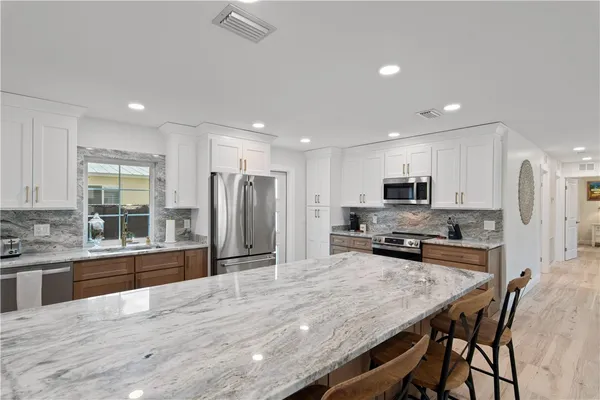 a kitchen with stainless steel appliances a stove a sink a refrigerator white cabinets and wooden floor