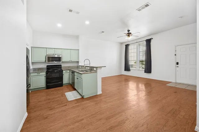 a kitchen with stainless steel appliances a stove top oven a sink dishwasher and a refrigerator with wooden floor