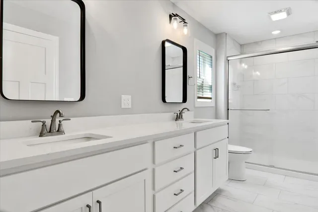 a bathroom with a double vanity sink toilet mirror and shower