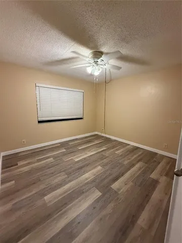 a view of an empty room with chandelier fan and wooden floor