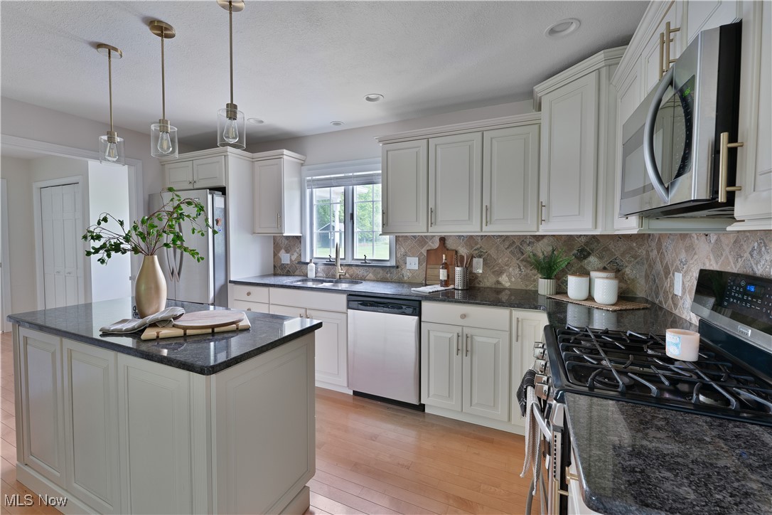 7091 South Raccoon Road Canfield, OH 44406 - Photo 13 of 39 Kitchen featuring appliances with stainless steel finishes, light wood-style floors, a kitchen island, tasteful backsplash, and pendant lighting