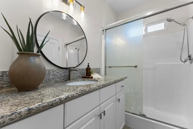 a bathroom with a granite countertop sink a mirror and shower